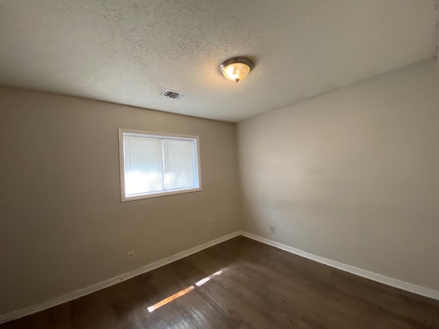 spare room featuring a textured ceiling and dark hardwood / wood-style flooring