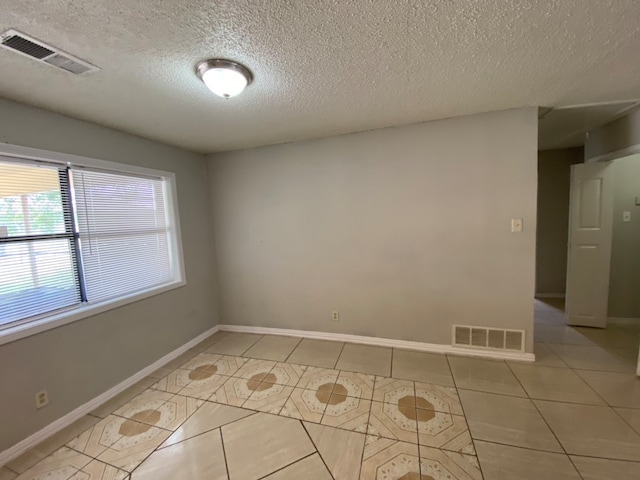 empty room with a textured ceiling and light tile patterned floors