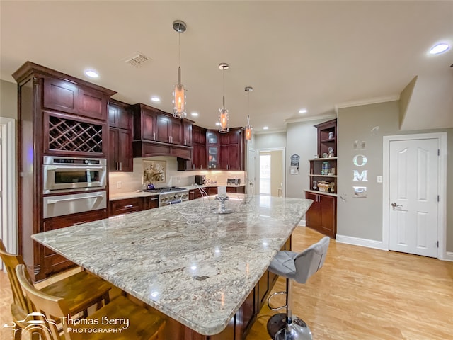 kitchen featuring a large island, pendant lighting, light hardwood / wood-style floors, appliances with stainless steel finishes, and ornamental molding