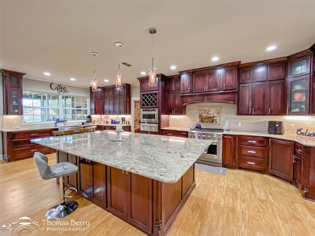 kitchen featuring appliances with stainless steel finishes, light stone countertops, pendant lighting, a center island, and light hardwood / wood-style flooring