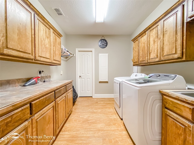 washroom with cabinets, light hardwood / wood-style floors, a textured ceiling, sink, and independent washer and dryer