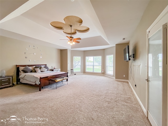 bedroom with ceiling fan, a raised ceiling, and light carpet