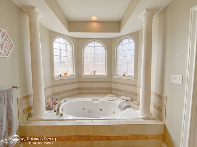 bathroom featuring a raised ceiling, tiled tub, and ornate columns