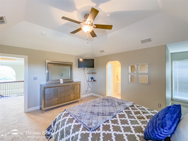 bedroom featuring ceiling fan, ensuite bath, a tray ceiling, and light carpet