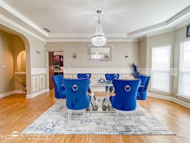 interior space featuring ornamental molding, wood-type flooring, a notable chandelier, and a raised ceiling