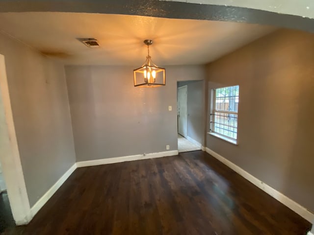 spare room with dark wood-type flooring and a chandelier