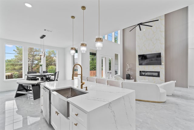 kitchen with white cabinetry, light stone countertops, plenty of natural light, decorative light fixtures, and a center island with sink