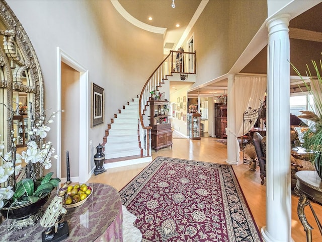 foyer featuring light wood-type flooring, decorative columns, ornamental molding, and a towering ceiling