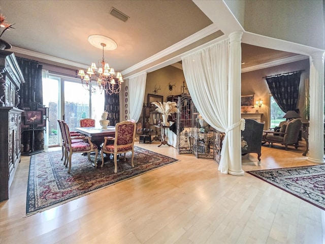 dining space with wood-type flooring, ornamental molding, a notable chandelier, and ornate columns