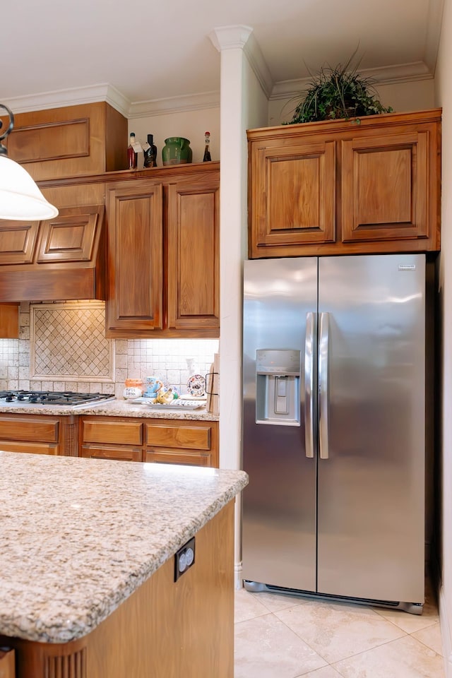 kitchen with appliances with stainless steel finishes, decorative backsplash, light tile patterned flooring, light stone countertops, and crown molding