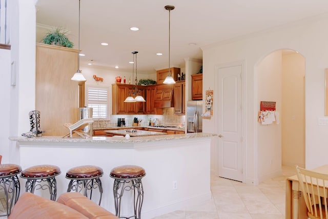 kitchen with kitchen peninsula, backsplash, appliances with stainless steel finishes, decorative light fixtures, and light stone countertops