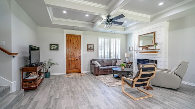 living room with light hardwood / wood-style floors, a fireplace, beamed ceiling, ceiling fan, and ornamental molding