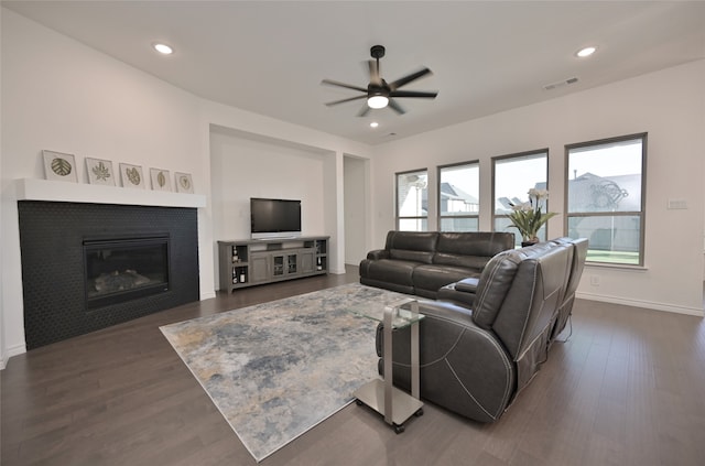 living room featuring a tile fireplace, dark hardwood / wood-style flooring, and ceiling fan