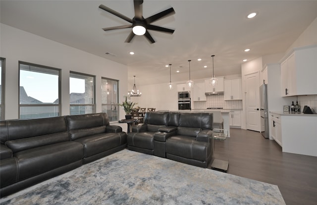 living room featuring ceiling fan with notable chandelier and dark wood-type flooring