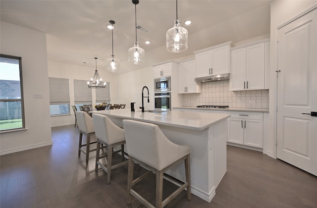 kitchen with an island with sink, appliances with stainless steel finishes, hanging light fixtures, and white cabinetry