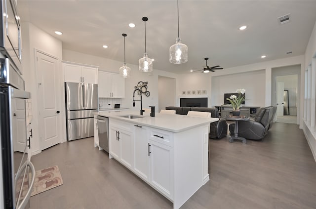 kitchen with stainless steel appliances, white cabinetry, ceiling fan, and a kitchen island with sink