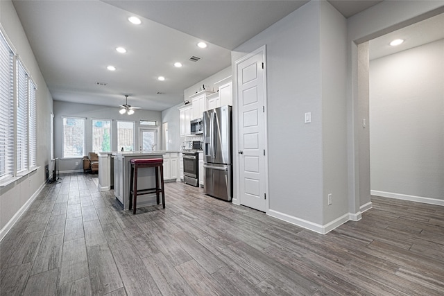 kitchen featuring ceiling fan, a breakfast bar, white cabinetry, stainless steel appliances, and a center island