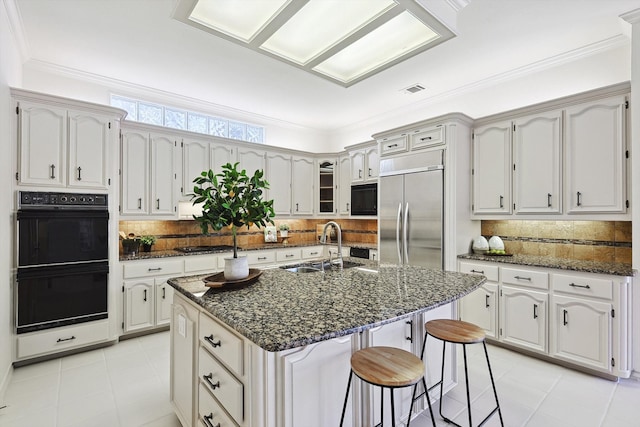 kitchen with sink, an island with sink, white cabinets, black appliances, and backsplash