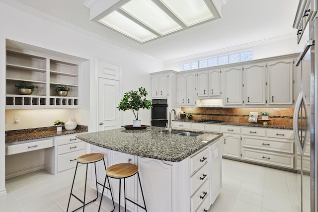 kitchen with a center island with sink, white cabinets, dark stone counters, ornamental molding, and sink