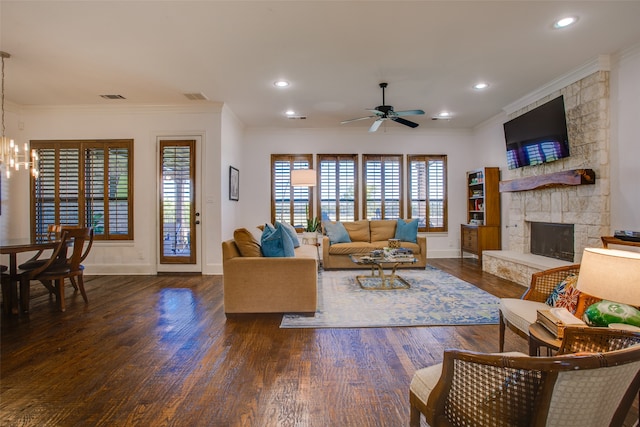 living room with ceiling fan with notable chandelier, dark hardwood / wood-style floors, ornamental molding, and a stone fireplace