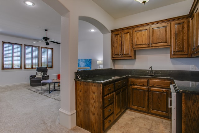 kitchen with dark stone countertops, ceiling fan, light carpet, and kitchen peninsula