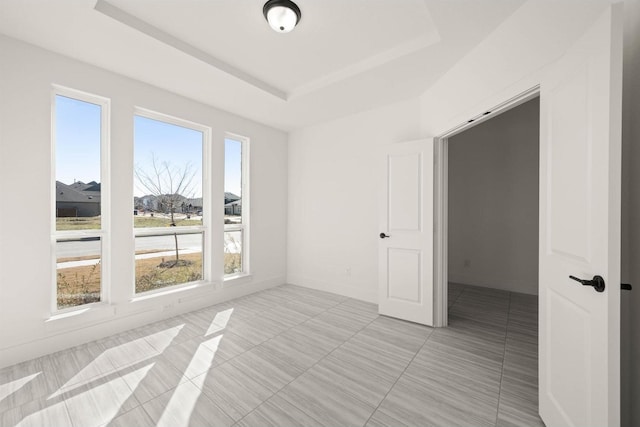 tiled empty room featuring a raised ceiling