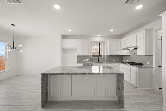 kitchen with a kitchen island, stainless steel gas stovetop, sink, white cabinets, and light stone countertops