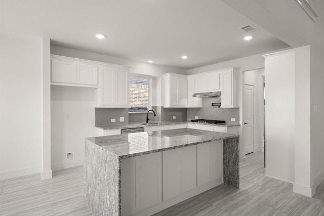 kitchen featuring sink, white cabinetry, stainless steel appliances, light stone counters, and a kitchen island