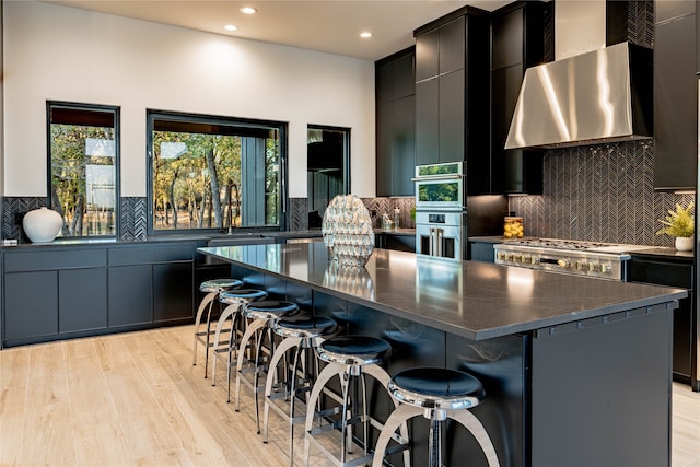 kitchen with wall chimney exhaust hood, a breakfast bar, light hardwood / wood-style floors, and a kitchen island