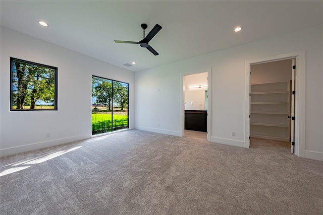 unfurnished bedroom featuring a closet, access to exterior, light carpet, a walk in closet, and ceiling fan