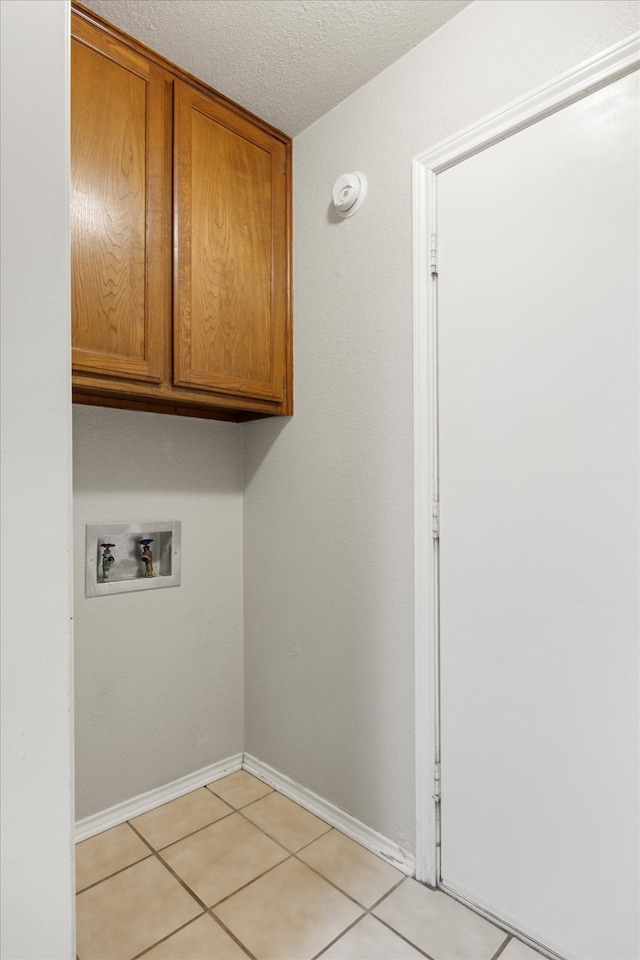 clothes washing area with washer hookup, cabinets, light tile patterned floors, and a textured ceiling