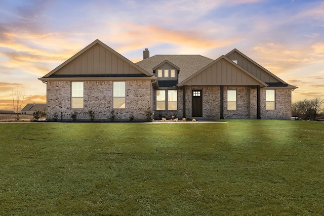 view of front of house featuring brick siding, a chimney, board and batten siding, and a yard