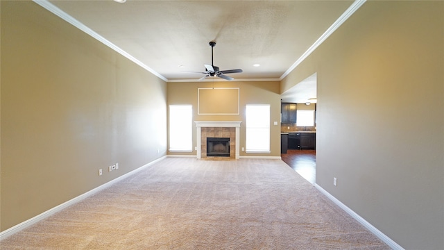 unfurnished living room with crown molding, carpet flooring, a tiled fireplace, and ceiling fan