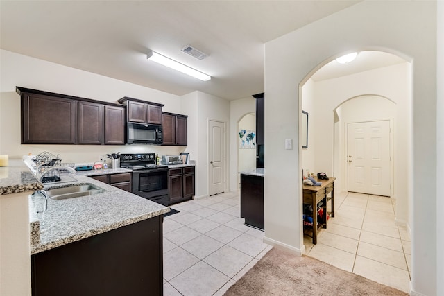 kitchen with dark brown cabinets, sink, black appliances, light tile patterned floors, and light stone countertops