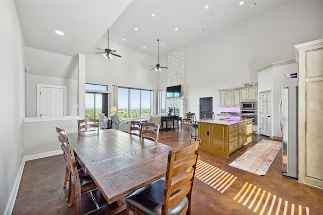 dining space with a stone fireplace, a high ceiling, and ceiling fan