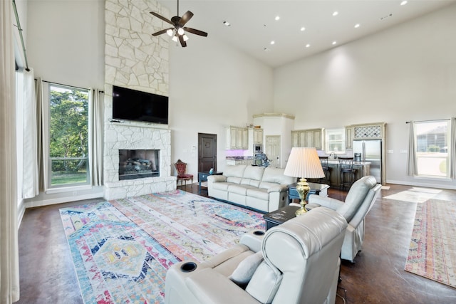 living room with ceiling fan, a fireplace, and a towering ceiling