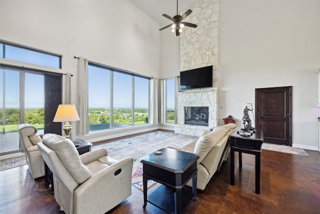 living room featuring ceiling fan, a stone fireplace, and a towering ceiling