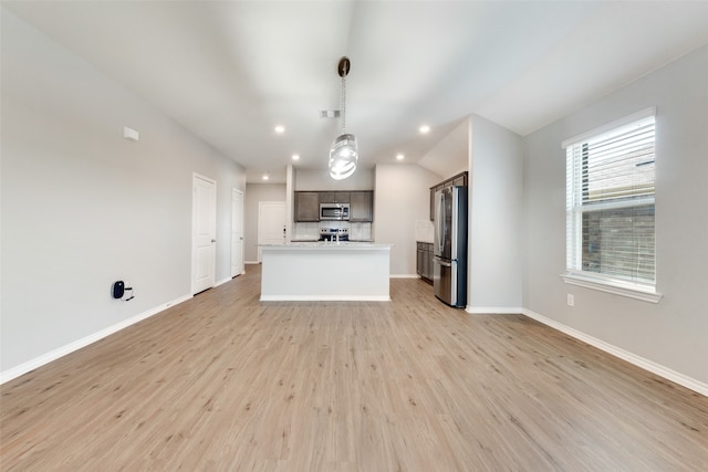 kitchen featuring vaulted ceiling, stainless steel appliances, light hardwood / wood-style flooring, decorative light fixtures, and a kitchen island with sink