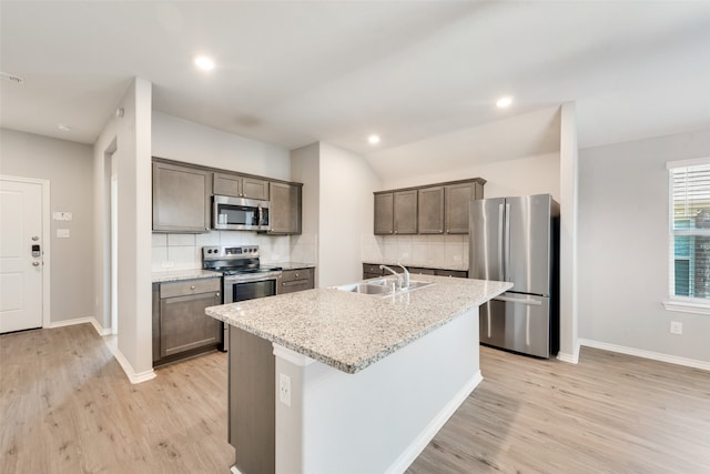 kitchen with light stone counters, sink, light hardwood / wood-style flooring, stainless steel appliances, and a center island with sink