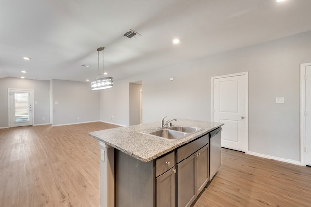 kitchen featuring hanging light fixtures, light stone counters, light hardwood / wood-style flooring, a center island with sink, and sink