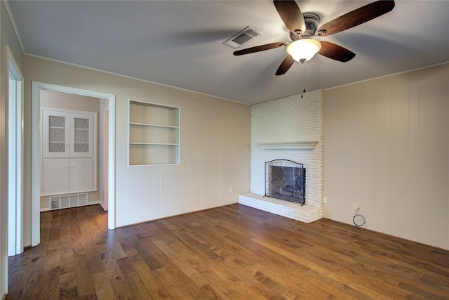 unfurnished living room with dark wood-type flooring, a fireplace, ceiling fan, built in shelves, and ornamental molding