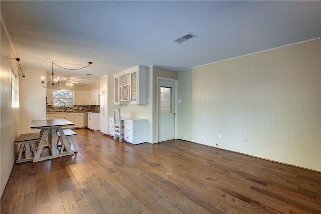 unfurnished living room featuring ornamental molding, dark hardwood / wood-style floors, sink, and a notable chandelier