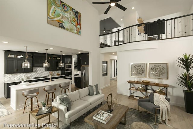 living room with ceiling fan, sink, light hardwood / wood-style flooring, and a high ceiling