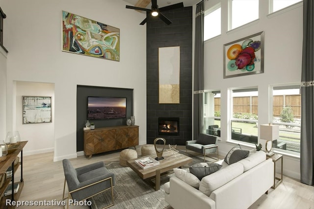 living room featuring a tile fireplace, light hardwood / wood-style floors, a towering ceiling, and ceiling fan