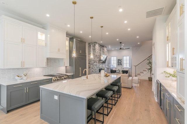 kitchen featuring tasteful backsplash, visible vents, light stone countertops, gray cabinetry, and light wood-style floors