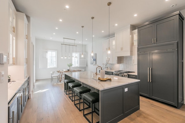 kitchen featuring paneled built in fridge, decorative backsplash, a large island, light wood-type flooring, and white cabinetry