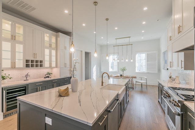 kitchen featuring wine cooler, visible vents, white cabinetry, appliances with stainless steel finishes, and a large island with sink