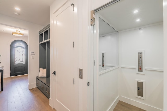 hallway featuring elevator, light wood-style flooring, arched walkways, and recessed lighting