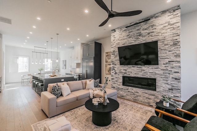 living area with visible vents, a ceiling fan, hardwood / wood-style flooring, a stone fireplace, and recessed lighting