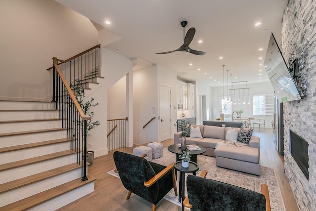 living area featuring recessed lighting, stairway, a ceiling fan, a stone fireplace, and light wood-type flooring